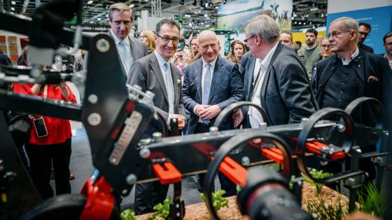 Bundesminister Özdemir beim Eröffnungsrundgang der Grünen Woche an einem Stand mit einem landwirtschaftlichen Roboter