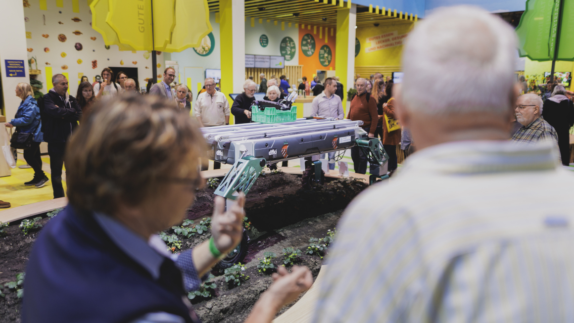 Besucher bertrachten in der Messehalle ein kleines Erdbeerfeld, auf dem ein Ernteroboter fährt.