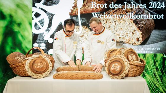 Der Bundesminister schneidet mit Roland Ermer, Präsident des Zentralverbands des Deutschen Bäckerhandwerks, ein Brot an, dahinter der Schriftzug - Brot des Jahres 2024 - Weizenvollkornbrot