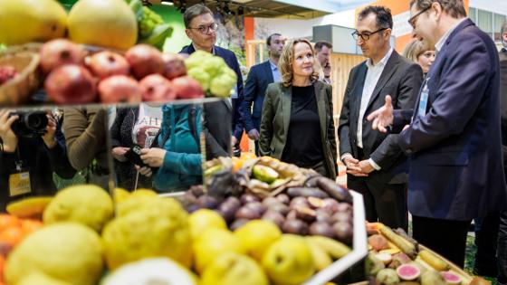 Bundesminister Özdemir und Bundesministerin Lemke stehen im Gespräch in der Messehalle an einem Gestand mit verschiedenen Obstsorten 