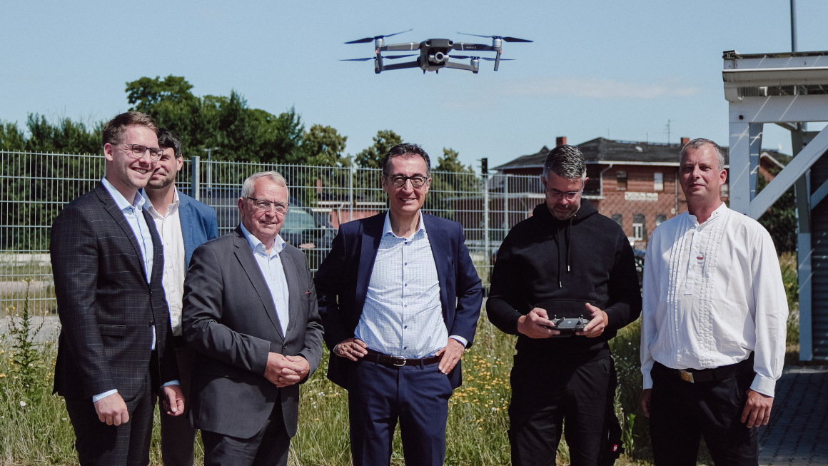 Gruppenbild Bundesminster Özdemir mit seinem Kollegen Backhaus aus Mecklenburg-Vorpommern und Mitarbeitern der Dachdeckerfirma, über ihnen fliegt eine Drohne der Firma