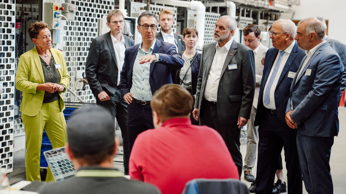 Bundesminster Özdemir steht in einer Gruppe in einem Berufsbildungszentrum. Im Gegenüber sitzen Auszubildende.