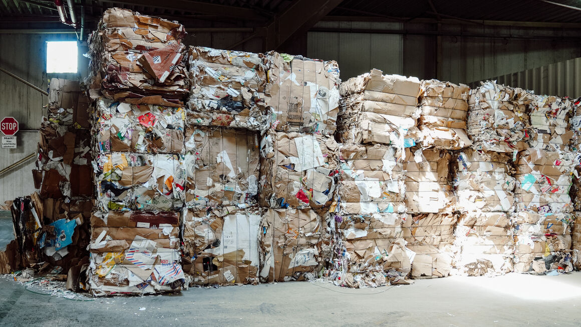 Blick auf mehrere quadratisch gepresste Blöcke aus Recyclingmaterial in einer Halle.