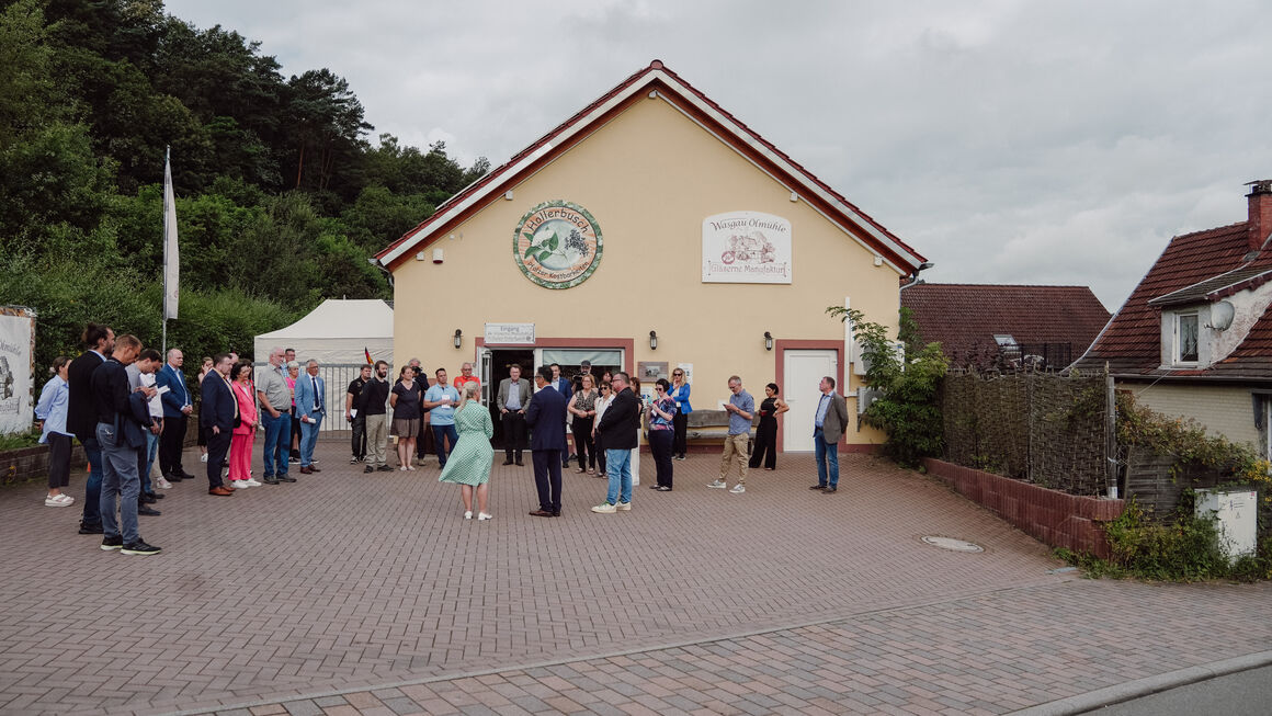 Blick auf die Ölmühle, eine umgebaute Turnhalle, davor steht Bundeminister Özdemir mit vielen Personen