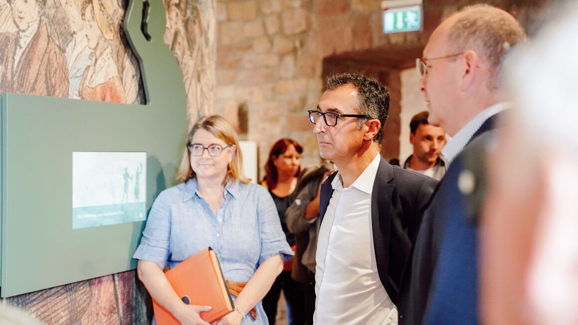 Bundesminister Cem Özdemir steht mit mehreren Personen vor einer Informationstafel im Hambacher Schlossmuseum.