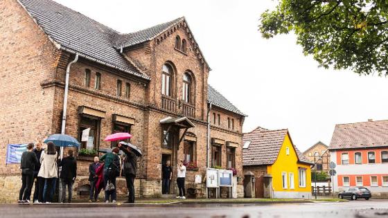 Gebäude des Dorftreffs, davor Menschen mit Regenschirmen.