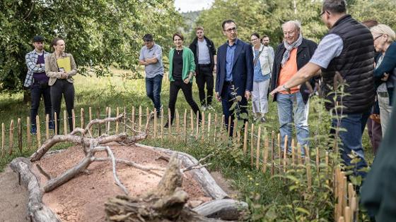 Führung durch die Naturstation: Bundesminister Cem Özdemir und eine Menschengruppe stehen vor einer abgezäunten Insekteninsel.