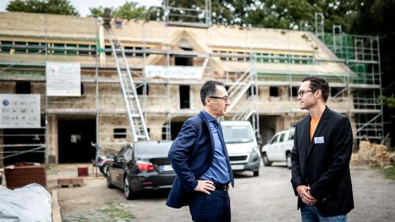 Bundesminister Cem Özdemir im Gespräch, im Hintergrund ein ehemaliger Pferdestall im Baugerüst.