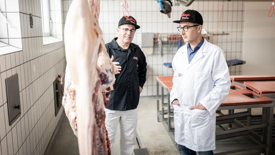 Bundesminister Özdemir mit Metzger, vor ihnen hängen geschlachtete Tiere