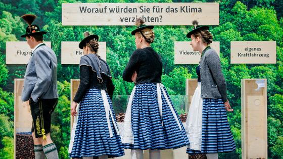 Ein Abstimm-Modul auf der IGW: 4 Besucherinnen und Besucher in Trachten stimmen gerade mittels Kastanien ab: "Worauf würden Sie für das Klima verzichten?" Möglichkeiten sind: Flugreisen, Fleisch, Videostreaming, eigenes Kraftfahrzeug.