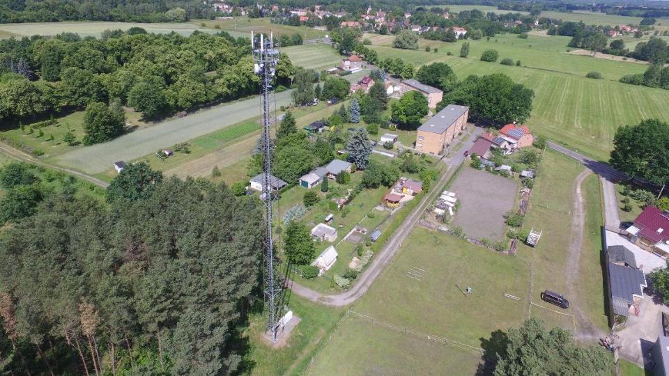 Funkmast in einer ländlichen Region mit Feldern, Bäumen und Gebäuden