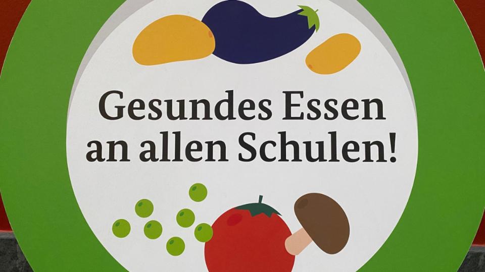 Kappaplatte in Form eines Tellers, auf dem Gemüse zu sehen ist. Zudem die Schrift: Gesundes Essen an allen Schulen!