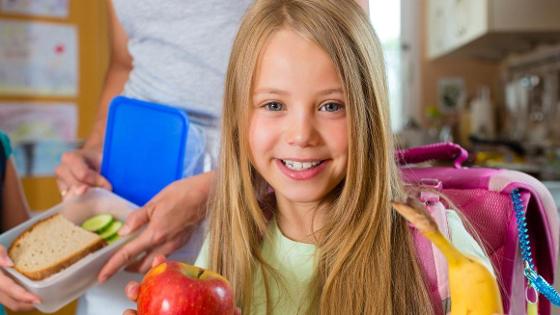 Kind zeigt Apfel und Banane, Im Hintergrund steht die Mutter