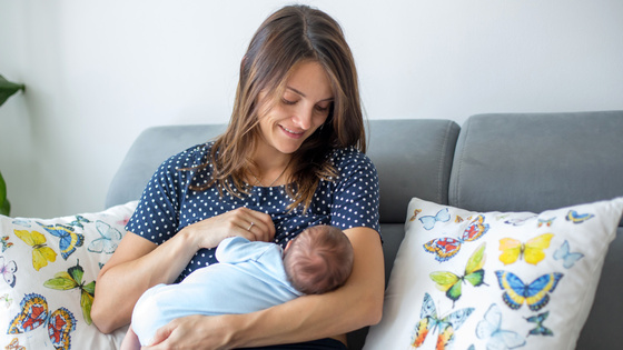 Eine Frau sitzt auf einem Sofa und stillt ihr Baby