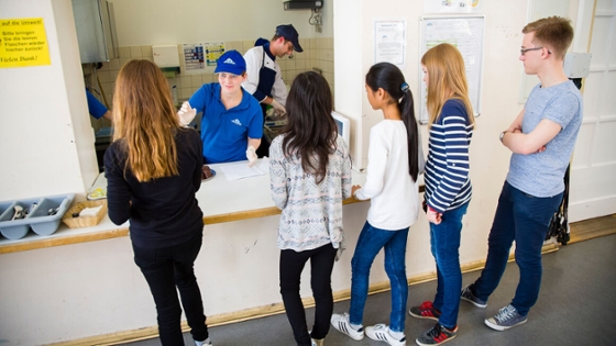 Schülerinnen und Schüler stehen an der Essensausgabe in der Schule an