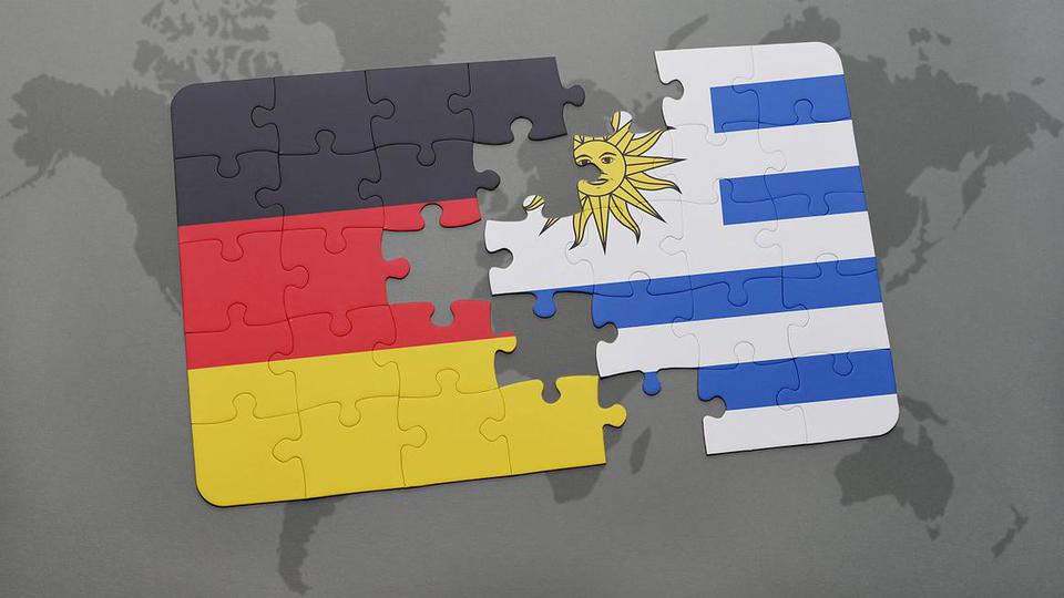 Die Landesflaggen von Uruguay und Deutschland als stilisiertes Puzzle, das auf einer Weltkarte liegt.