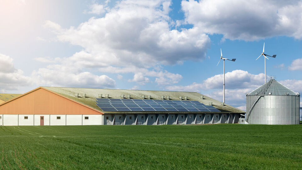 Stall mit Solaranlage, Windrädern, Silos hinter einen Feld mit Grünland