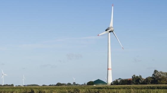 im Vordergrund eine Windkraftanlage auf einem Feld, im Hintergrund eine Biogasanlage und weitere Windräder