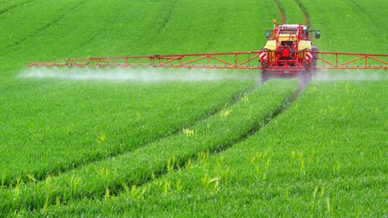 Traktor mit Pflanzenschutzspritze fährt über ein Feld