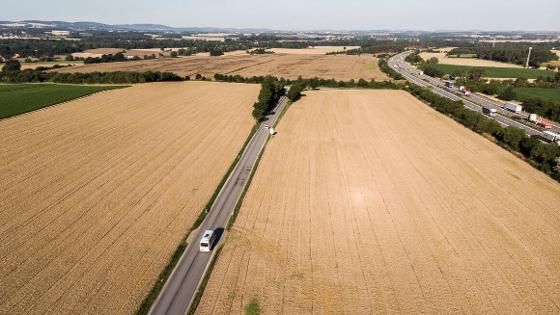 Blick von oben auf Felder, die von einer Autobahn und einer Straße durchzogen sind