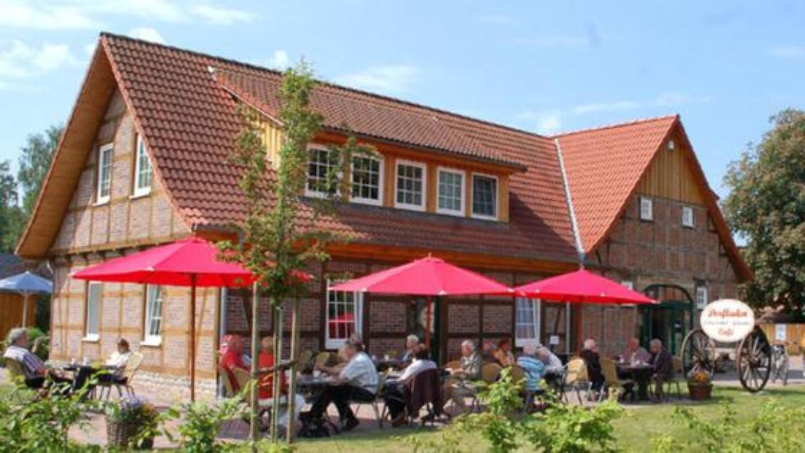  Fachwerkgebäude mit Außengastronomie; im Vordergrund Menschen, die unter roten Sonnenschirmen sitzen.  