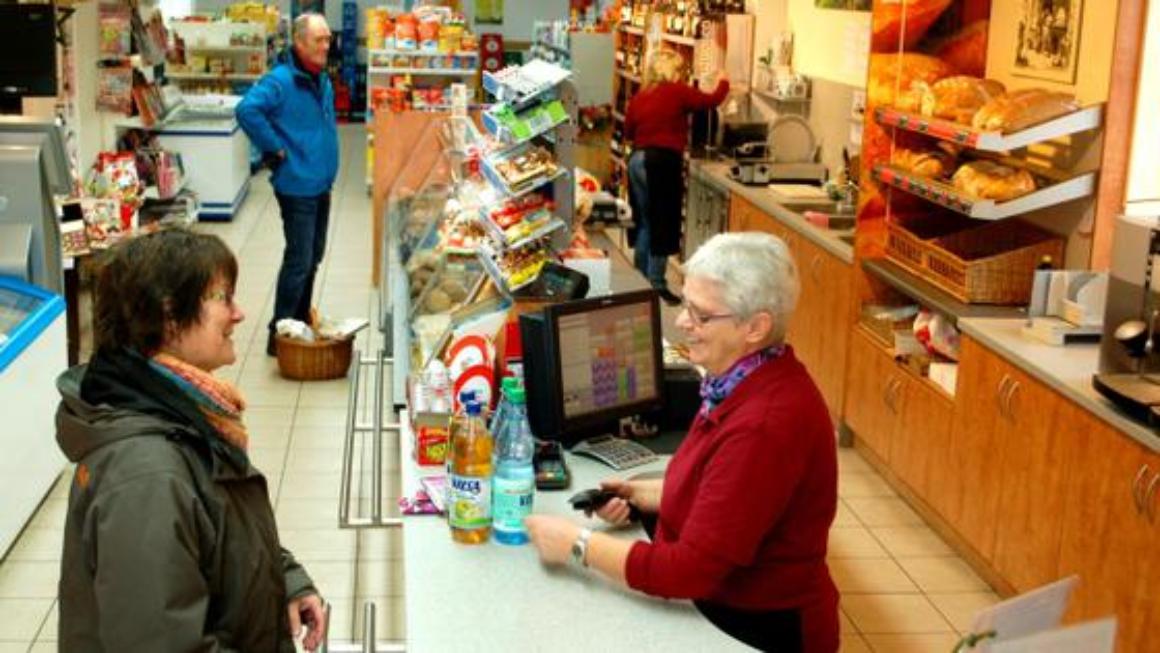 Zwei Verkäuferinnen bedienen in einem kleinen Dorfladen zwei Kunden. 