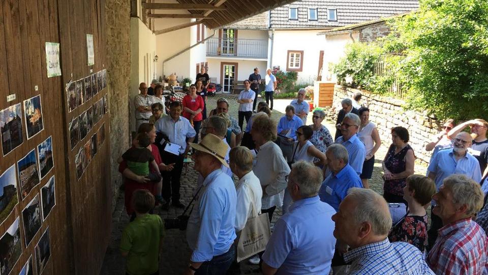 Fotos sind an einer Wand aufgeklebt, davor Personen, die die Bilder betrachten 