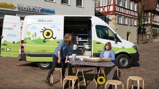 Zwei Frauen haben vor einem Lieferwagen, dem sog. KulTourMobil, einen Tisch und Stühle aufgebaut.