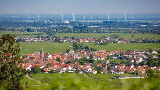 Im Vordergrund ein Dorf, im Hintergrund ein Windpark