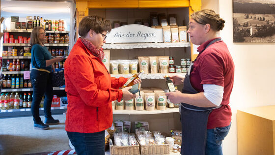 In a store, a customer and a saleswoman stand in front of a shelf with the inscription "Aus der Region" ("From the region")