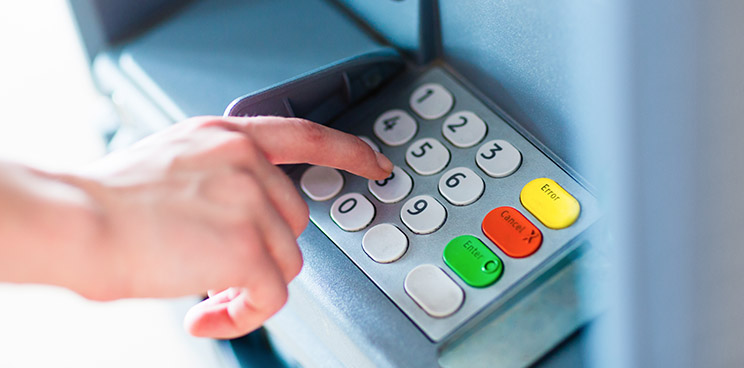 A hand typing on an ATM keypad.