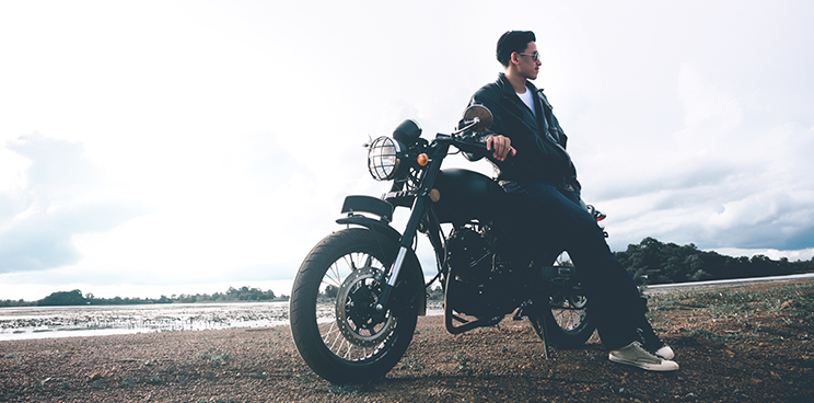 A man leaning on his bike on a dirt road