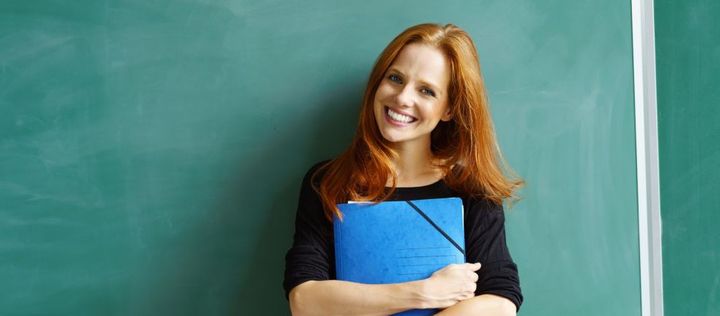 Lehrerin steht vor einer Tafel mit Block in den Händen