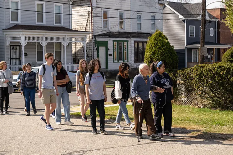 Elderly gentleman with cane leads group of students through neighborhood