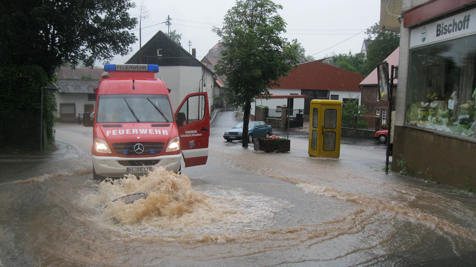 Flood water pushes up a manhole cover. A fire engine in the background.