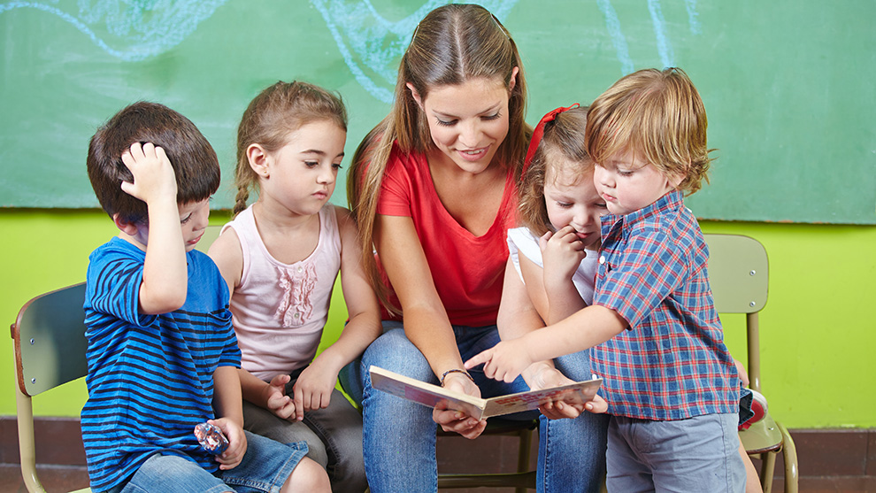 Kinder und Erzieherin lesen Buch im Kindergarten | Quelle: © Robert Kneschke / Adobe Stock