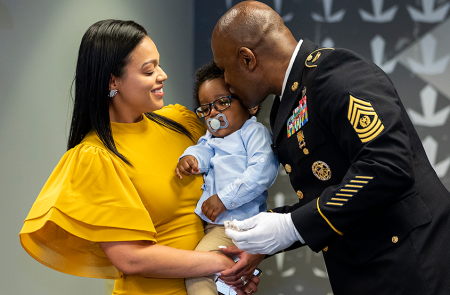 Woman holding a baby being kissed by veteran.