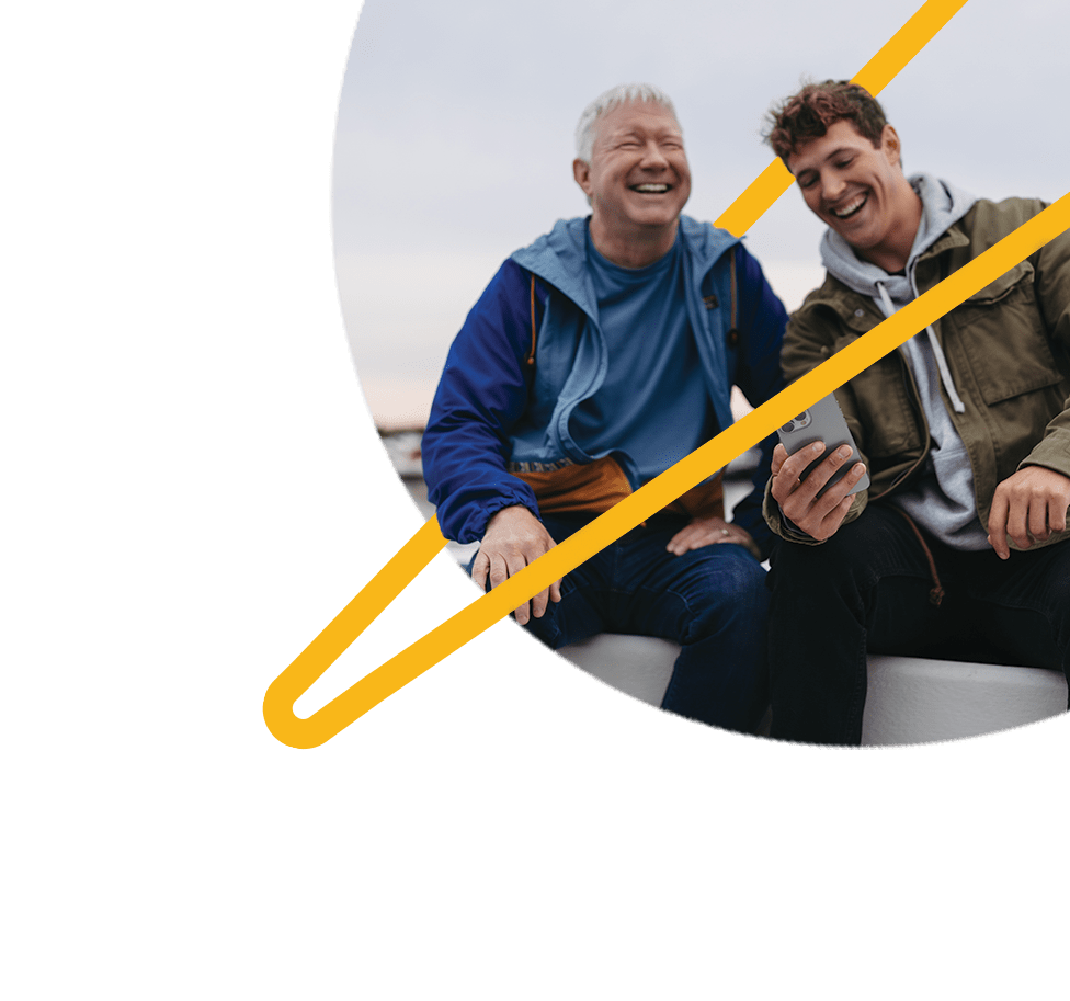 An older man and a young man looking at a phone and laughing together.