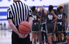 A ref holding a basketball with players in the background