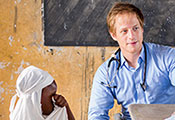 Dr Cameron Gaskill with stethoscope around his neck sitting next to a child