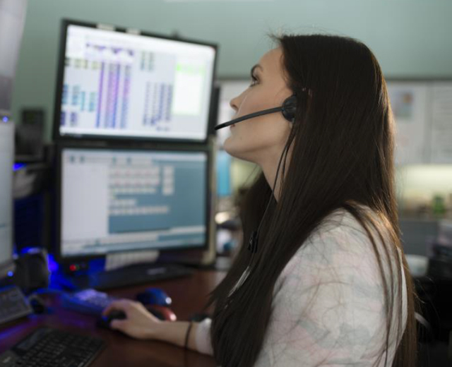 911 operator with headset, hand on mouse, and scanning 4 different screens