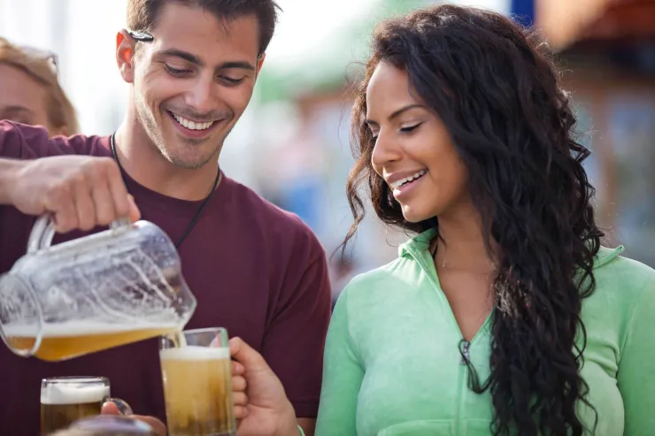 A man pours a beer from a pitcher for his friend