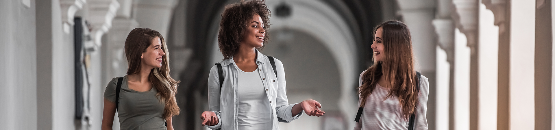  three college-aged women talking while walking down a corridor 