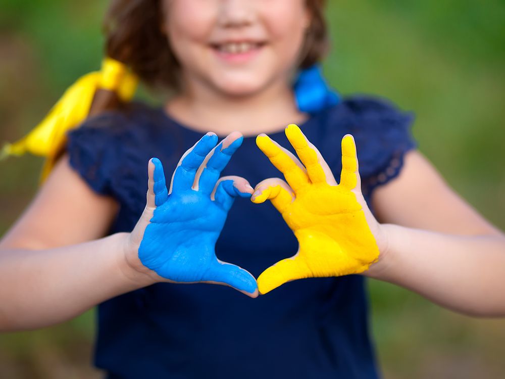 Das Bild zeigt ein Kind, das seine Handflächen zeigt. Die eine ist blau, die andere gelb ind den Farben der Ukraine bemalt.