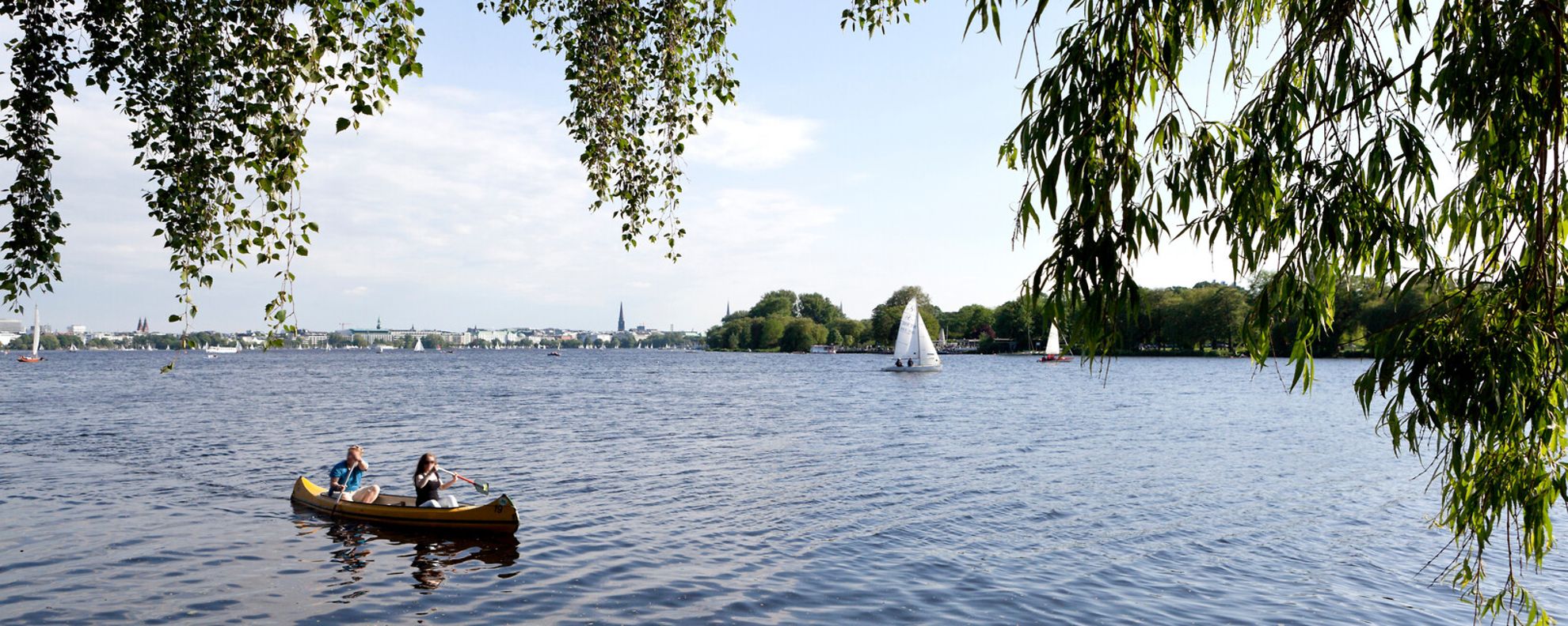 Ein Kanu und ein paar Segelboote fahren auf der Außenalster.