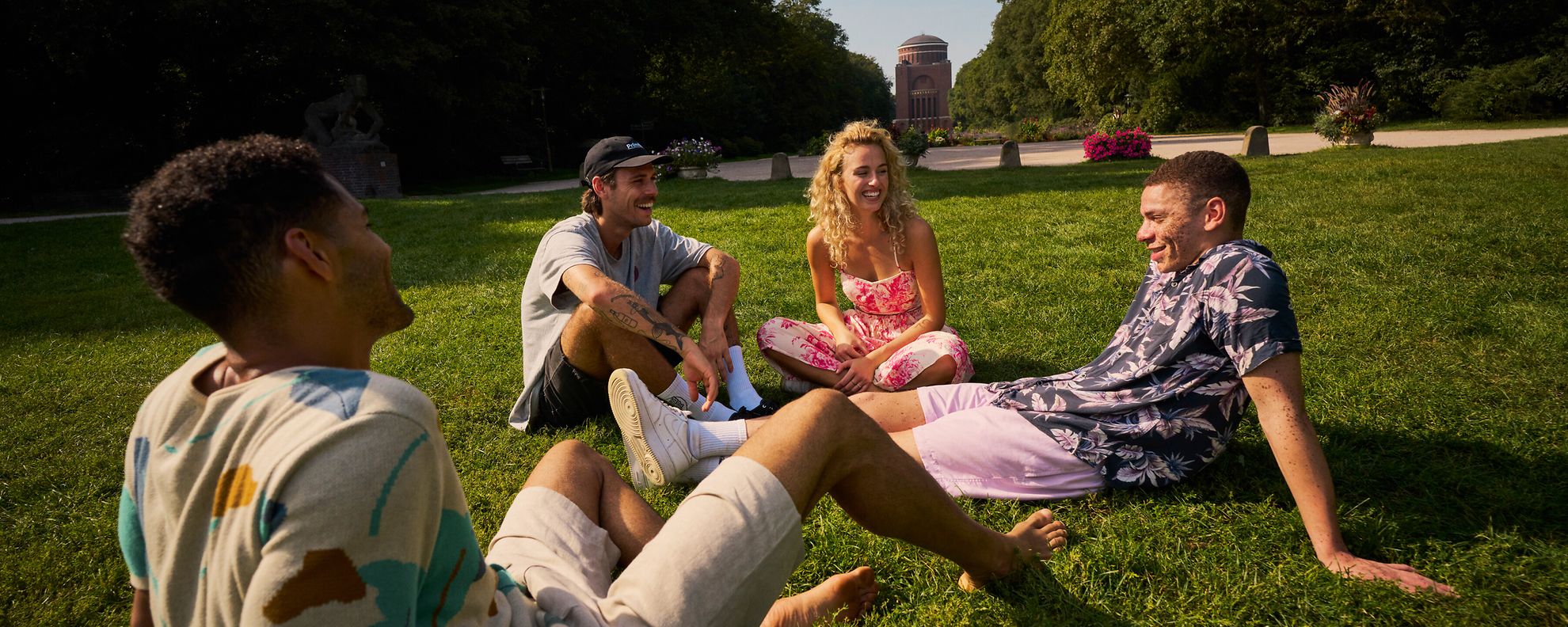 Mehrere Personen sitzen in einem Park auf der Wiese und unterhalten sich.