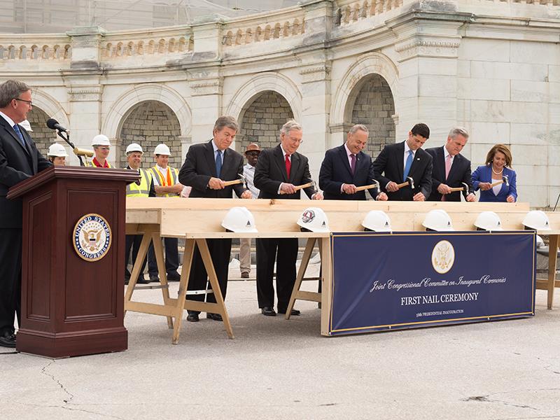 Seven people are hammering a nail into a piece of wood as Stephen T. Ayers looks on