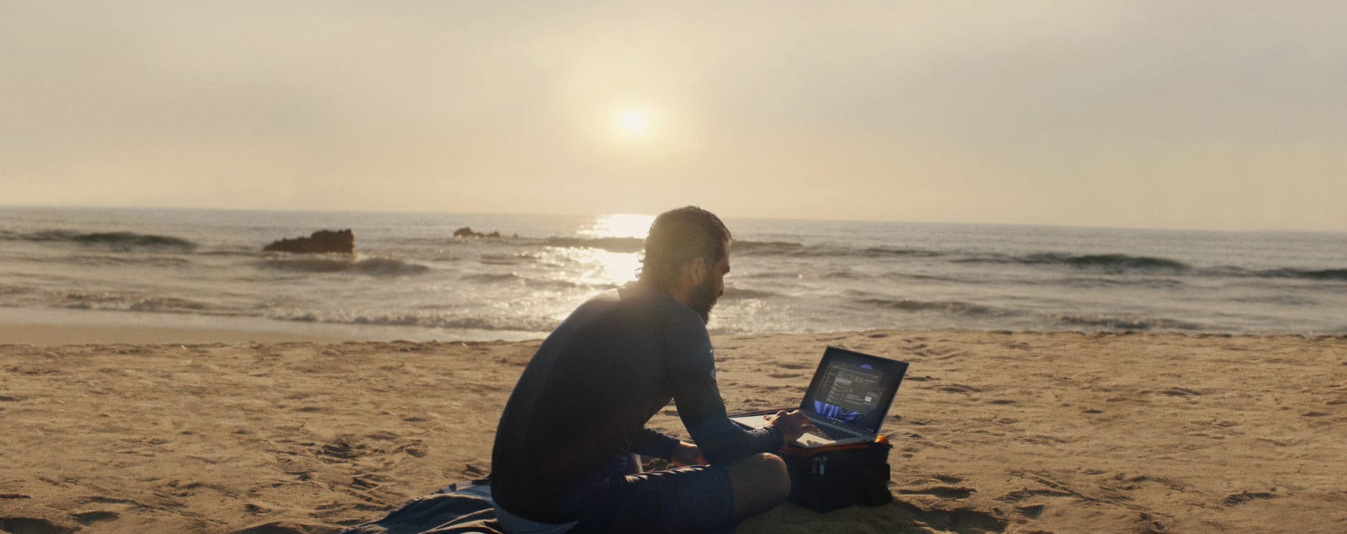 Man working on HP laptop, on a beach at sunset