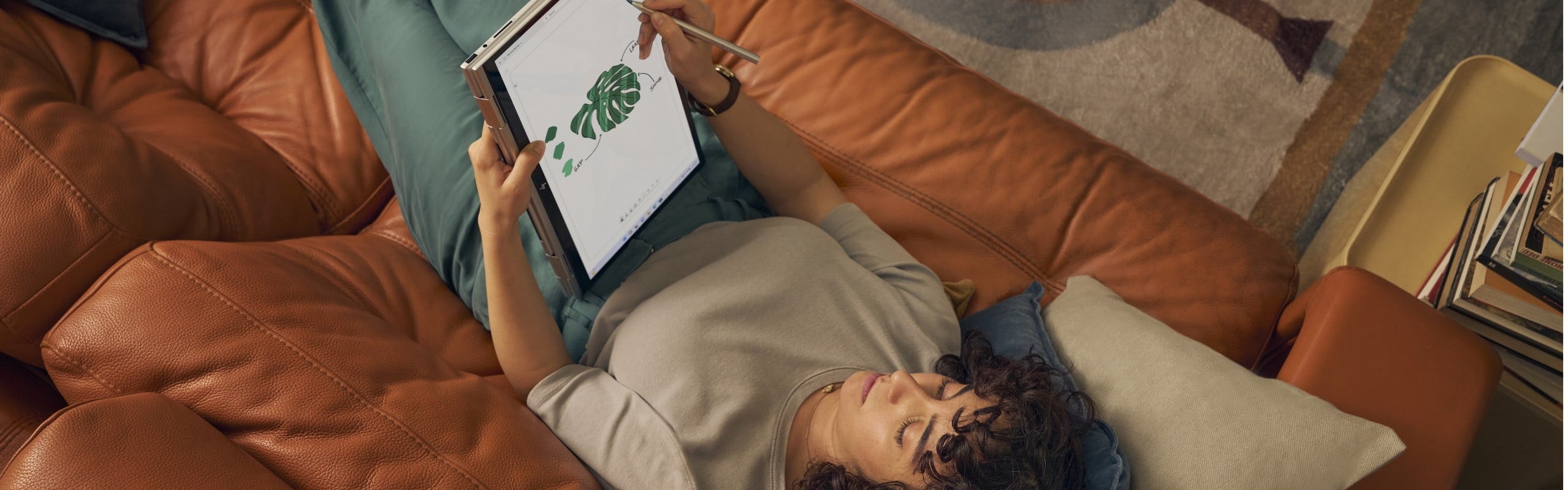 A woman drawing on her HP laptop in tablet mode while laying on her couch.