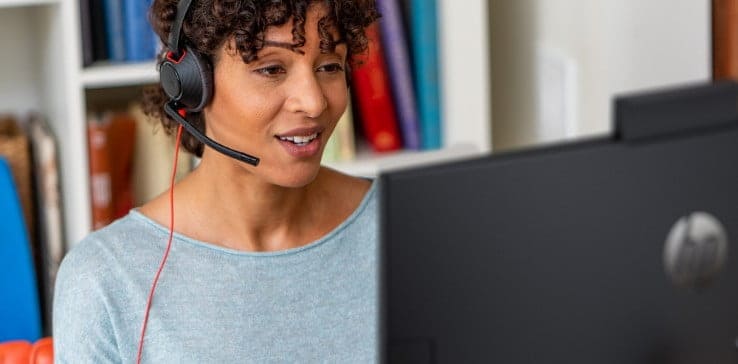 Woman wearing Poly Blackwire wired headset, seated at home office desk and engaged in a video call